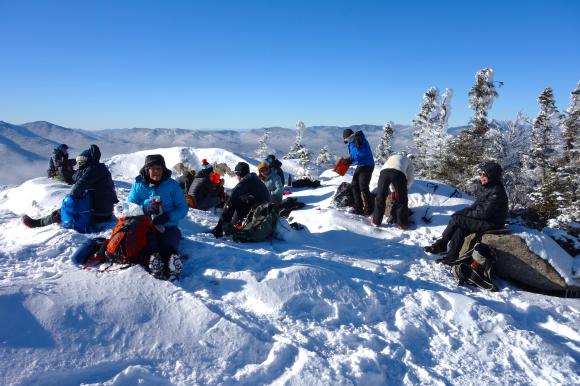 Crooked Canes snowshow hikers enjoy lunch together on an Adirondack mountain during a winter outing.